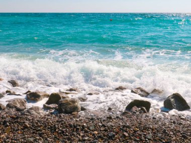 Şeffaf deniz dalgaları ve dinlenmek için kayalık bir plaj.