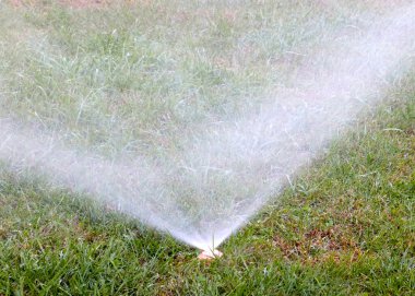 Çimleri plastik spreyle sularken su akar.
