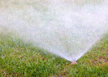 Çimleri plastik spreyle sularken su akar.