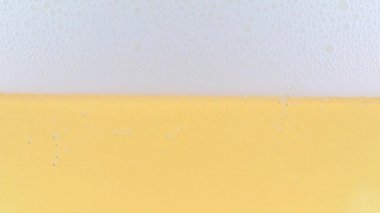Yüzeydeki köpükte bir bardak hafif bira ve hava kabarcıkları.
