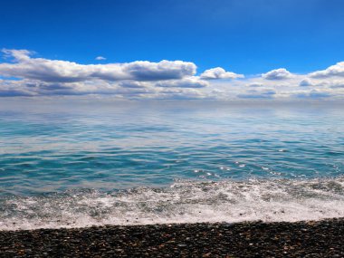 Güzel, güneşli bir yer ve kayalık bir sahilde deniz dalgaları.