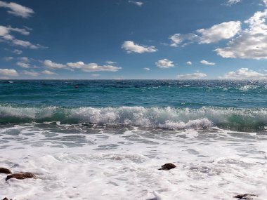 Güneşli bulutlu gökyüzünün altında muhteşem dalgalar ve çakıl taşı deniz plajı