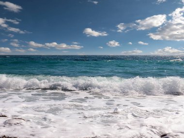 Güneşli bulutlu gökyüzünün altında muhteşem dalgalar ve çakıl taşı deniz plajı
