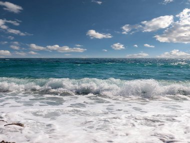 Güneşli bulutlu gökyüzünün altında muhteşem dalgalar ve çakıl taşı deniz plajı