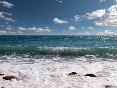 Güneşli bulutlu gökyüzünün altında muhteşem dalgalar ve çakıl taşı deniz plajı
