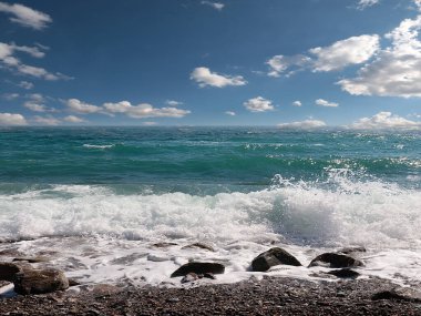 Güneşli bulutlu gökyüzünün altında muhteşem dalgalar ve çakıl taşı deniz plajı