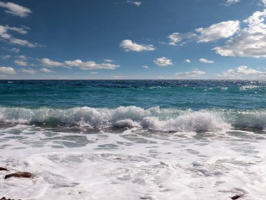 Güneşli bulutlu gökyüzünün altında muhteşem dalgalar ve çakıl taşı deniz plajı
