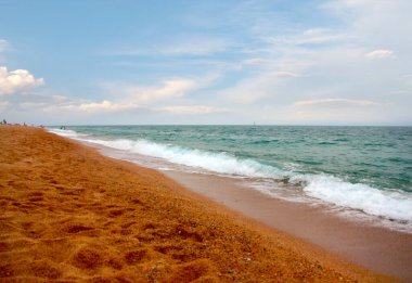 Kumlu sahili ve güneşli gökyüzü olan güzel bir deniz manzarası.