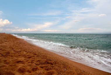 Kumlu sahili ve güneşli gökyüzü olan güzel bir deniz manzarası.