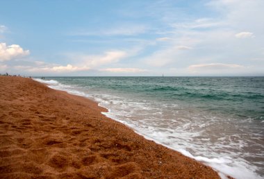 Kumlu sahili ve güneşli gökyüzü olan güzel bir deniz manzarası.