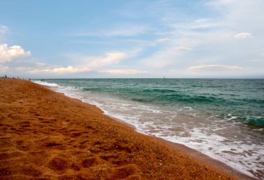 Kumlu sahili ve güneşli gökyüzü olan güzel bir deniz manzarası.