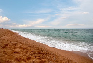 Kumlu sahili ve güneşli gökyüzü olan güzel bir deniz manzarası.