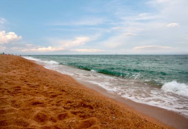 Kumlu sahili ve güneşli gökyüzü olan güzel bir deniz manzarası.
