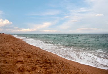 Kumlu sahili ve güneşli gökyüzü olan güzel bir deniz manzarası.