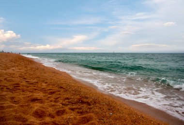Kumlu sahili ve güneşli gökyüzü olan güzel bir deniz manzarası.