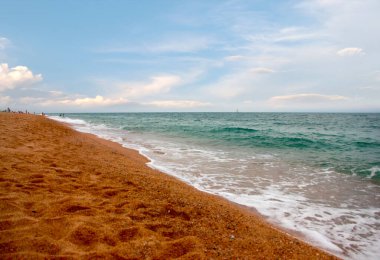 Kumlu sahili ve güneşli gökyüzü olan güzel bir deniz manzarası.