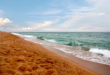 Kumlu sahili ve güneşli gökyüzü olan güzel bir deniz manzarası.