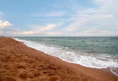 Kumlu sahili ve güneşli gökyüzü olan güzel bir deniz manzarası.