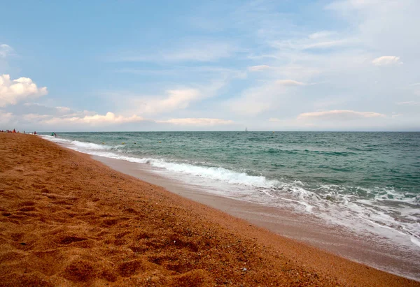Kumlu sahili ve güneşli gökyüzü olan güzel bir deniz manzarası.