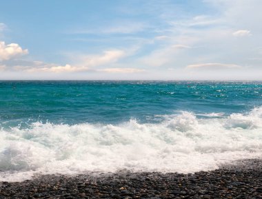 Çakıl taşı plajı ve güneşli gökyüzü olan güzel deniz manzarası.