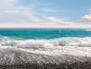 Çakıl taşı plajı ve güneşli gökyüzü olan güzel deniz manzarası.