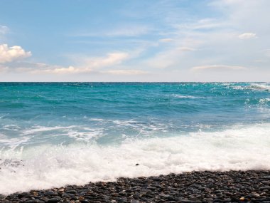 Çakıl taşı plajı ve güneşli gökyüzü olan güzel deniz manzarası.