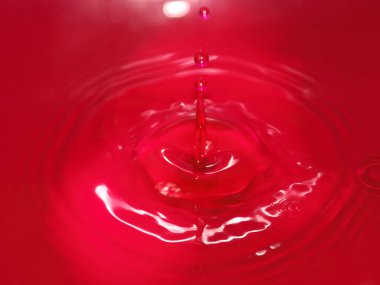 Bir damla kan kırmızı sıvı suyun yüzeyine düşer.