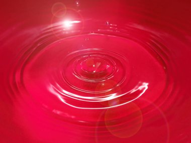 Bir damla kan kırmızı sıvı suyun yüzeyine düşer.