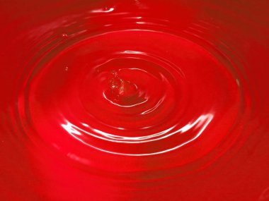 Bir damla kan kırmızı sıvı suyun yüzeyine düşer.