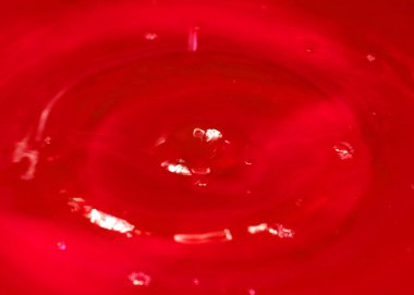 Bir damla kan kırmızı sıvı suyun yüzeyine düşer.