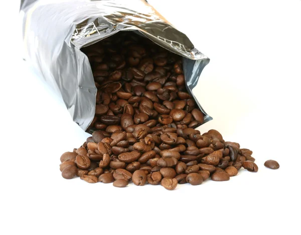Celá kávová zrna roztroušených na bílém pozadí s stříbrná balení Stock Snímky