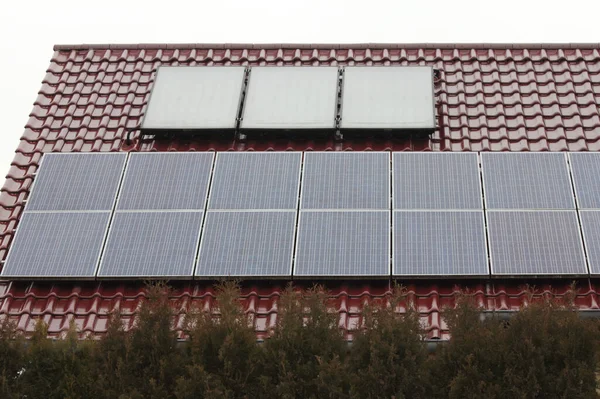 kırmızı boyanmış bir evin çatısındaki birçok güneş paneli