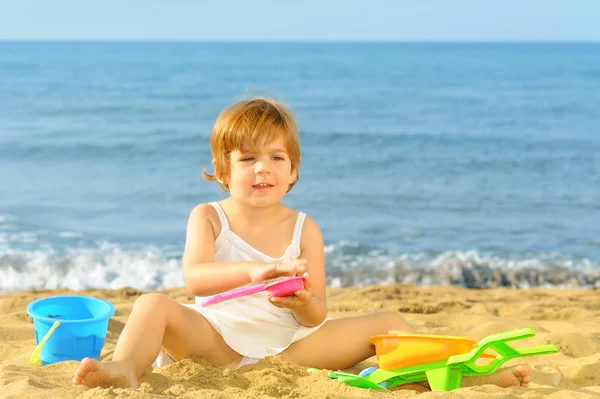 Счастливая девочка, играющая со своими игрушками на пляже — стоковое фото