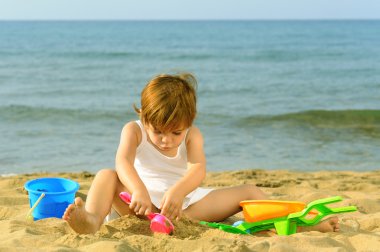 Kumsalda onun oyuncakları ile oynarken mutlu bebek kız
