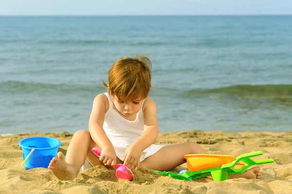 Счастливая девочка, играющая со своими игрушками на пляже — стоковое фото