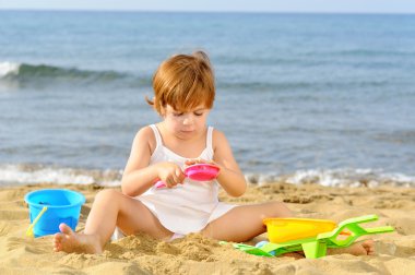 Kumsalda onun oyuncakları ile oynarken mutlu bebek kız
