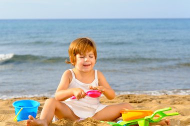 Kumsalda onun oyuncakları ile oynarken mutlu bebek kız