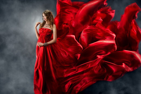 Beautiful woman in red waving silk dress as a flame. Looking down.