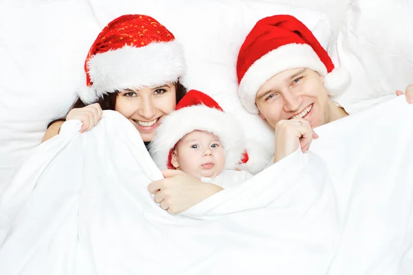 Οικογένεια Χριστούγεννα σε κόκκινα καπέλα ξαπλωμένη στο κρεβάτι λευκό — Φωτογραφία Αρχείου