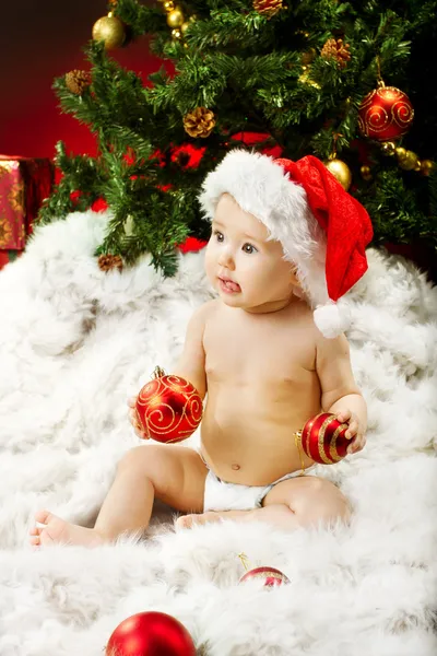 Weihnachtsbaby mit Hut sitzt auf Pelz und hält roten Ball — Stockfoto