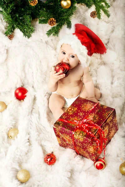 Weihnachtsbaby mit rotem Hut sitzt auf Pelz und isst Geschenk — Stockfoto