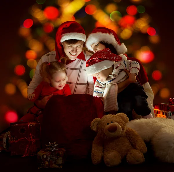 Família feliz de quatro pessoas em chapéus vermelhos abertura saco de iluminação — Fotografia de Stock