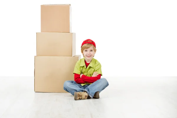 Niño sentado en frente de cajas de cartón pirámide . — Foto de Stock