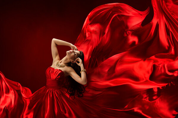 Woman in red dress blowing with flying fabric, fashion girl posing silk fluttering cloth