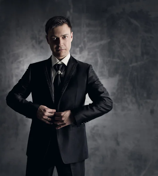 Schöner Mann im schwarzen Anzug. Bräutigam-Mode. grauer Hintergrund — Stockfoto