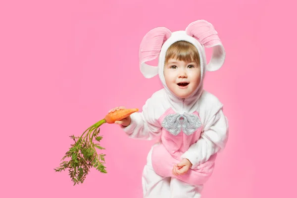 Bambino in costume da lepre coniglietto con carote in mano. Sfondo rosa — Foto Stock