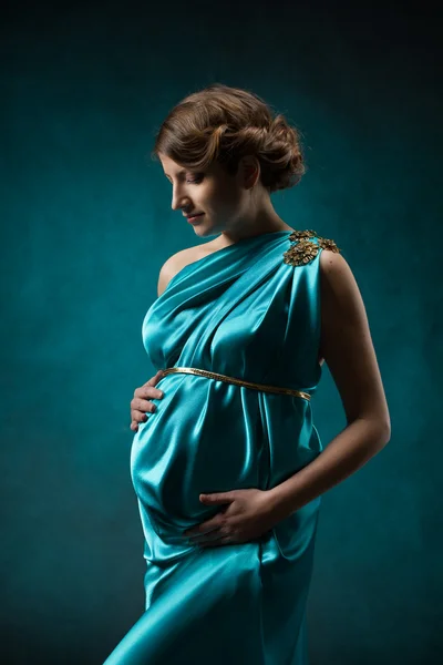 Gravid kvinna i långa siden klänning över blå art bakgrund. — Stockfoto