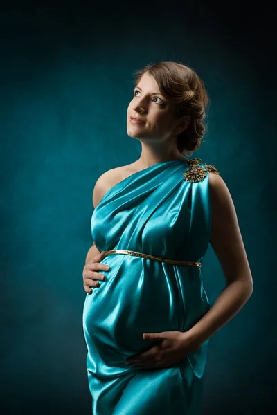 Pregnant woman in long silk dress over blue art background. — Stock Photo, Image