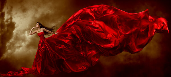 Woman in red waving beautiful dress with flying fabric, artistic sky