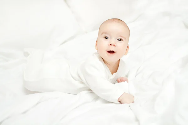 Gelukkig actieve baby liggend op maag boven witte bed. drie maanden — Stockfoto